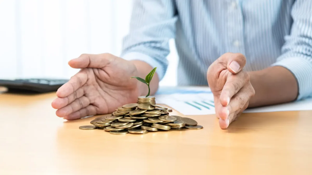 Main protégeant une pile de pièces avec une petite plante, symbolisant les aides financières aux entreprises et la gestion sécurisée des subventions.