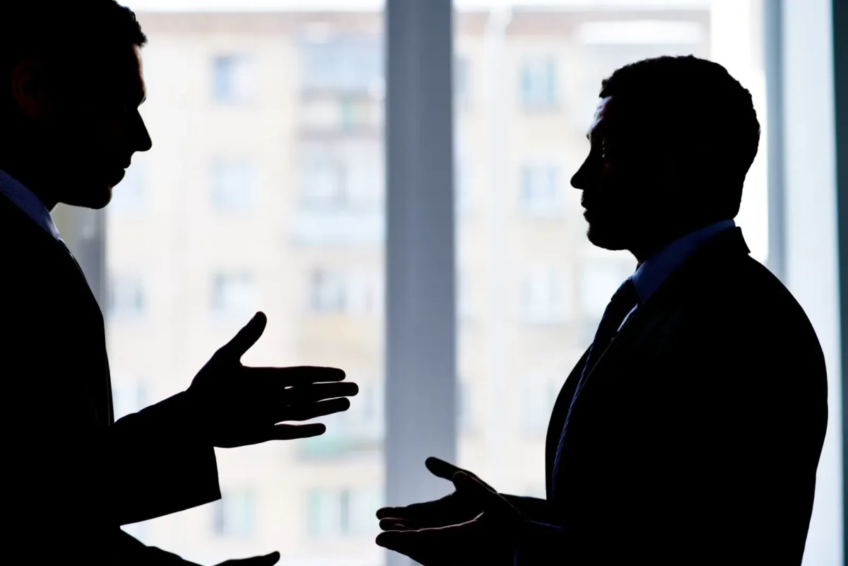 Deux hommes en costume discutant vivement dans un bureau, symbolisant un litige commercial ou une négociation de contrat tendue.